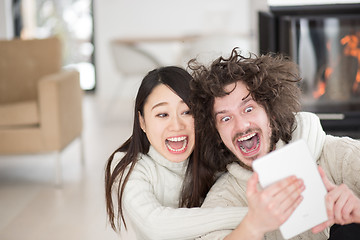 Image showing multiethnic couple using tablet computer in front of fireplace