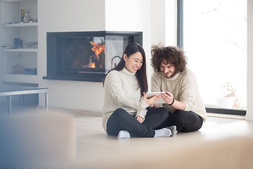 Image showing multiethnic couple using tablet computer in front of fireplace