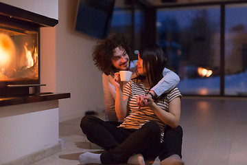 Image showing happy multiethnic couple sitting in front of fireplace