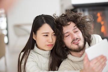 Image showing multiethnic couple using tablet computer in front of fireplace