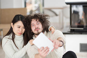 Image showing multiethnic couple using tablet computer in front of fireplace