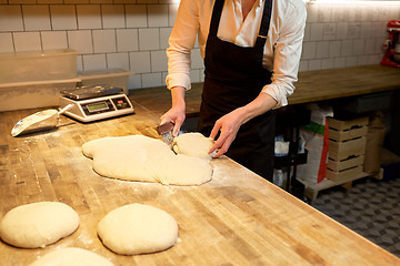 Image showing baker portioning dough with bench cutter at bakery