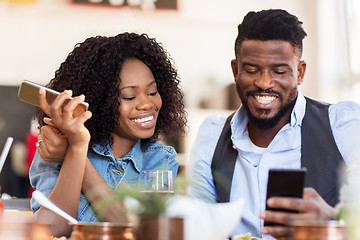 Image showing happy man and woman with smartphones at restaurant