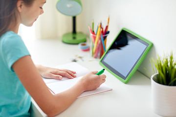 Image showing girl with tablet pc writing to notebook at home