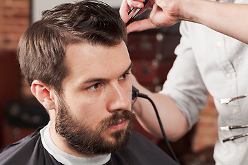 Image showing The hands of barber making haircut to young man in barbershop