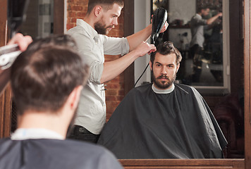 Image showing Young handsome barber making haircut of attractive man in barbershop