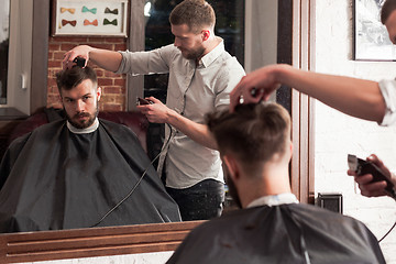 Image showing Young handsome barber making haircut of attractive man in barbershop