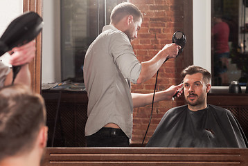 Image showing Young handsome barber making haircut of attractive man in barbershop