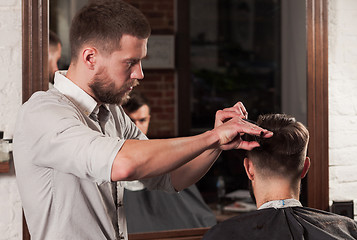 Image showing Young handsome barber making haircut of attractive man in barbershop