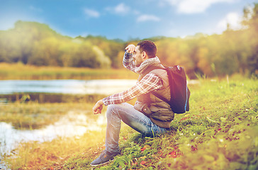 Image showing smiling man with backpack resting on river bank