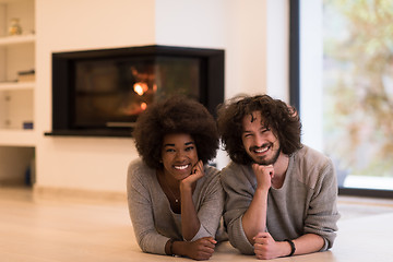 Image showing multiethnic couple lying on the floor  in front of fireplace