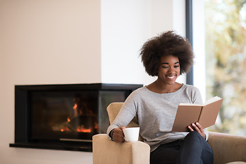 Image showing black woman reading book  in front of fireplace