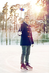 Image showing happy young man with smartphone on ice rink