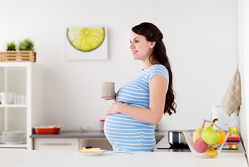 Image showing happy pregnant woman with mug and cake at home