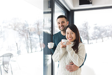 Image showing multiethnic couple enjoying morning coffee by the window