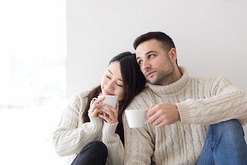 Image showing multiethnic couple enjoying morning coffee by the window