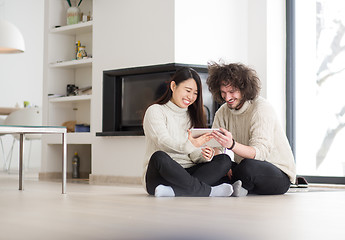 Image showing multiethnic couple using tablet computer in front of fireplace