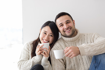 Image showing multiethnic couple enjoying morning coffee by the window