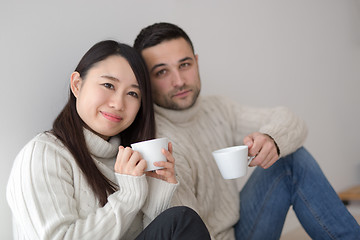 Image showing multiethnic couple enjoying morning coffee by the window