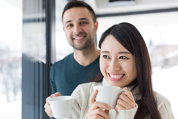 Image showing multiethnic couple enjoying morning coffee by the window