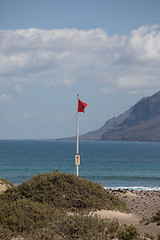 Image showing The red flag weighs in the wind at Surfers Beach Famara on Lanza