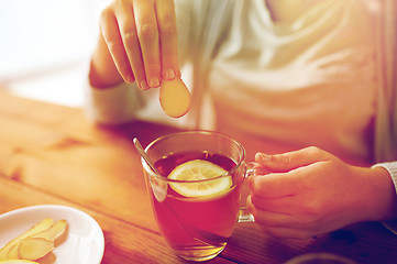 Image showing close up of woman adding ginger to tea with lemon