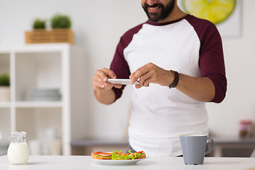 Image showing man photographing food by smartphone at home