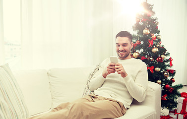 Image showing smiling man with smartphone at home for christmas