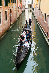 Image showing Venetian gondolier punting gondola through green canal waters of Venice, Italy