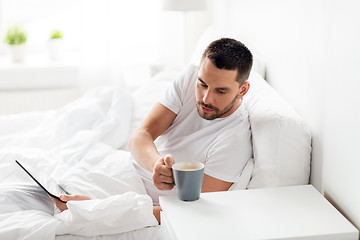Image showing man with tablet pc drinking coffee in bed at home