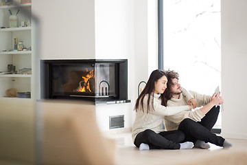 Image showing multiethnic couple using tablet computer in front of fireplace