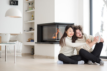 Image showing multiethnic couple using tablet computer in front of fireplace