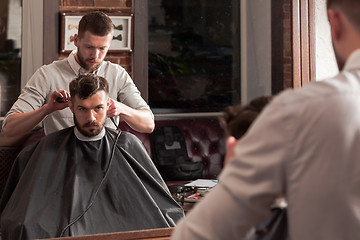 Image showing Young handsome barber making haircut of attractive man in barbershop