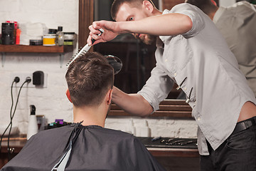 Image showing Young handsome barber making haircut of attractive man in barbershop