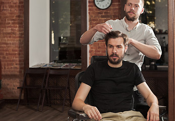 Image showing Young handsome barber making haircut of attractive man in barber