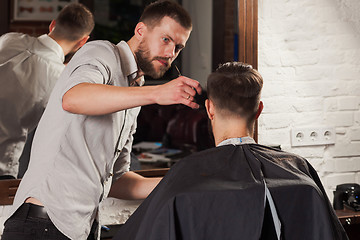 Image showing Young handsome barber making haircut of attractive man in barbershop