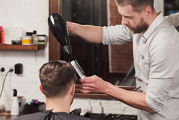 Image showing Young handsome barber making haircut of attractive man in barbershop