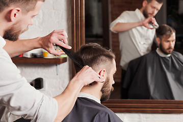 Image showing Young handsome barber making haircut of attractive man in barbershop