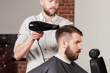 Image showing Young handsome barber making haircut of attractive man in barbershop