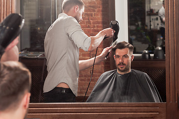 Image showing Young handsome barber making haircut of attractive man in barbershop