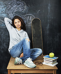 Image showing young cute teenage girl in classroom at blackboard seating on table smiling, modern hipster concept, lifestyle people