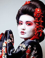 Image showing young pretty geisha in black kimono among sakura, asian ethno close up