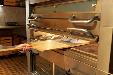 Image showing baker hand putting dough into bread oven at bakery