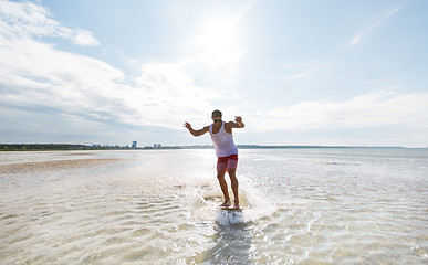 Image showing young man riding on skimboard on summer beach