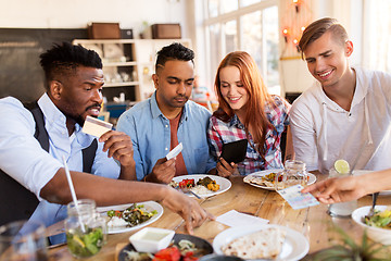 Image showing happy friends with money paying bill at restaurant