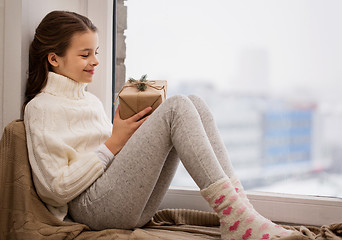 Image showing girl with christmas gift sitting on sill at home