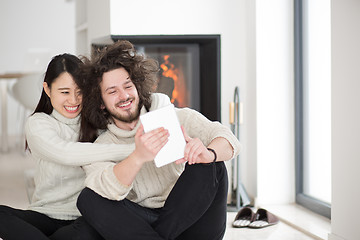 Image showing multiethnic couple using tablet computer in front of fireplace