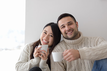 Image showing multiethnic couple enjoying morning coffee by the window