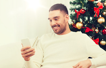 Image showing smiling man with smartphone at home for christmas