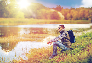 Image showing man with backpack resting on river bank